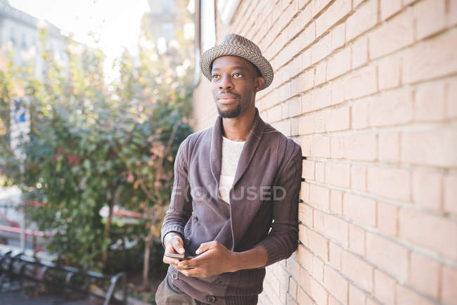 Man with smartphone leaning against brick wall — Stock Photo