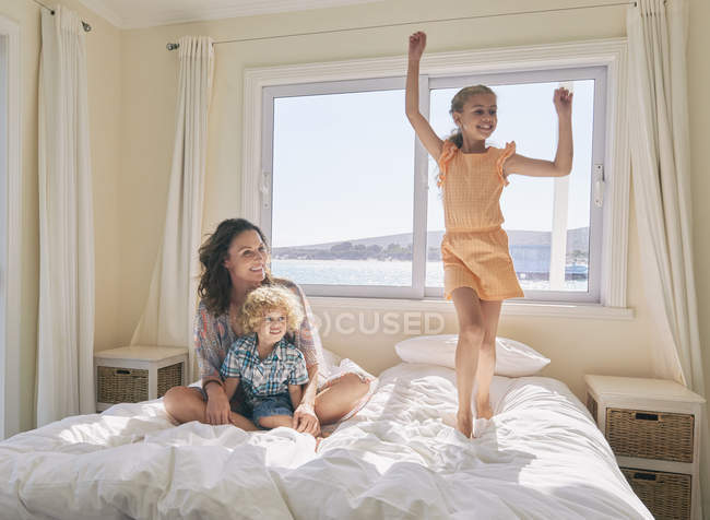 Mother and son watching girl jumping on bed — Stock Photo