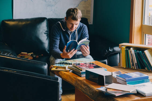Homem adulto médio sentado na cadeira, olhando através de livros — Fotografia de Stock