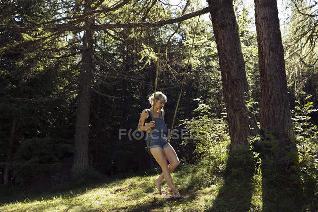 Femme moyenne adulte assise sur une balançoire forestière, Sattelbergalm, Tyrol, Autriche — Photo de stock