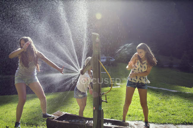 Drei erwachsene Freundinnen spielen Kampf mit Wasserschlauch im Garten — Stockfoto