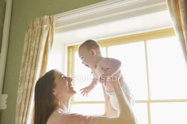 Mid adult woman holding up baby daughter in bedroom — Stock Photo