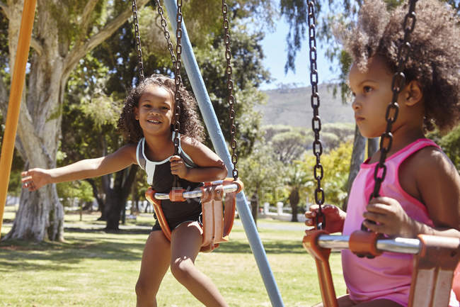 Due giovani sorelle che giocano sulle altalene del parco — Foto stock