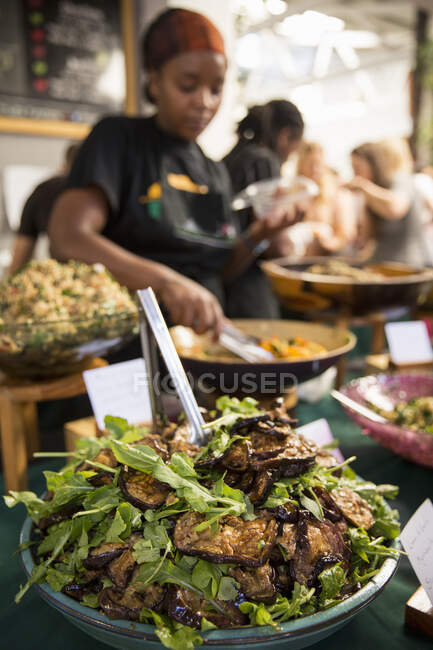 Ständerhalter serviert Auberginen-Salat am Stand der Genossenschaft — Stockfoto