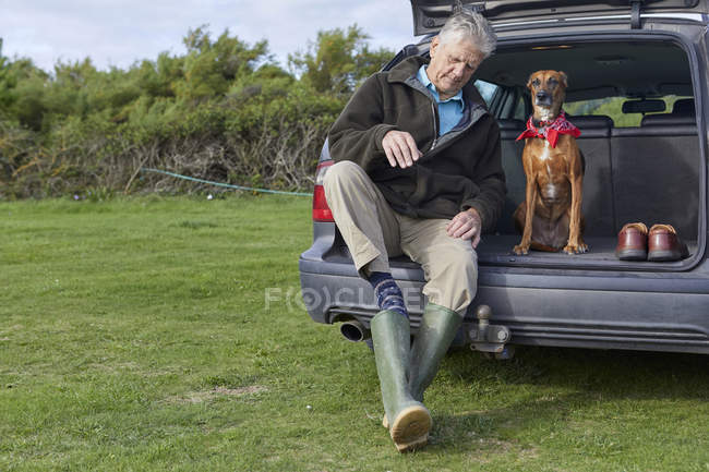 Uomo e cane seduti nel bagagliaio della macchina rimuovere stivali wellington — Foto stock