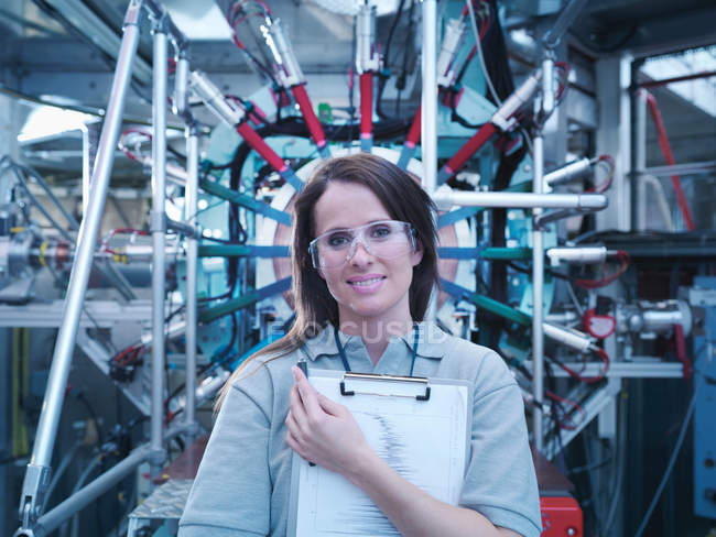 Female scientist with clipboard in front of particle accelerator — Stock Photo