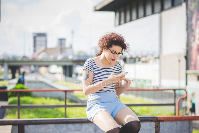 Frau sitzt im urbanen Raum und schreibt SMS auf Smartphone, Mailand, Italien — Stockfoto