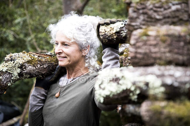 Reife Frau trägt Baumstamm auf der Schulter im Garten — Stockfoto