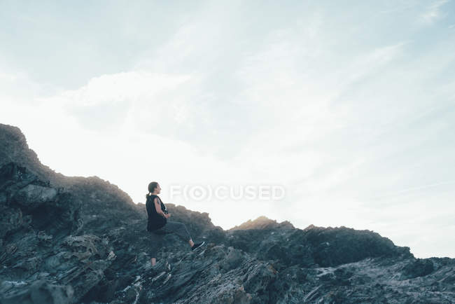Вид сбоку женщины, сидящей на скалах и отводящей взгляд, Стинтино, Сассари, Италия — стоковое фото
