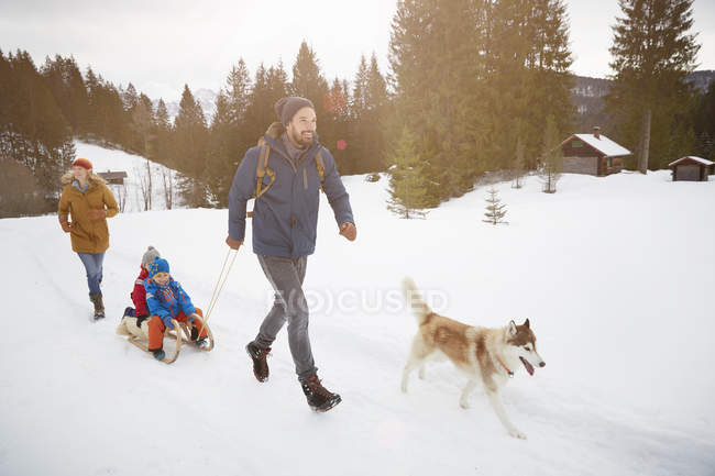 Parents with husky pulling sons on toboggan in snow covered landscape, Elmau, Bavaria, Germany — Stock Photo