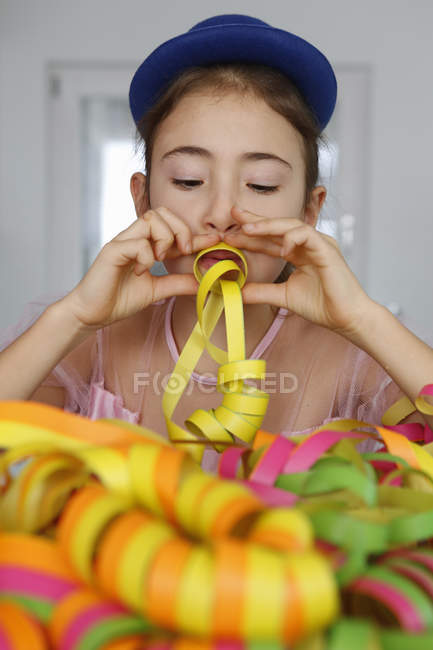 Chica vistiendo sombrero azul mirando hacia abajo soplando serpentinas fiesta - foto de stock