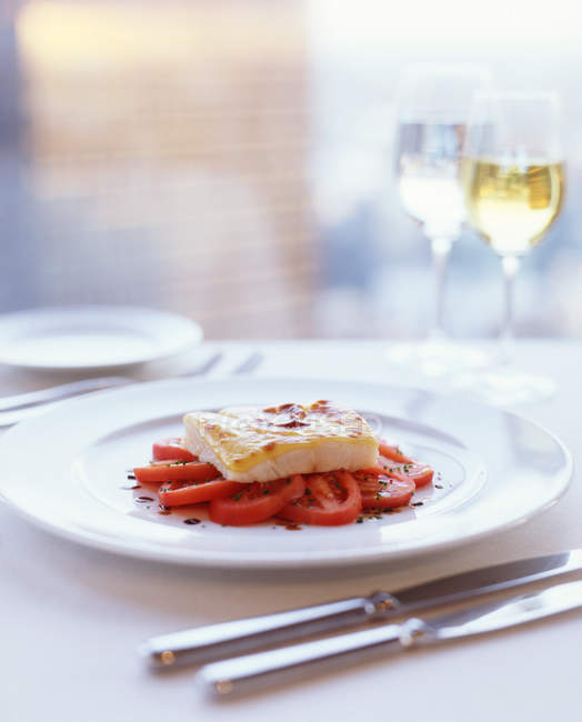Filet de poisson garni de fromage fondu sur lit de tomates fraîches assaisonnées — Photo de stock