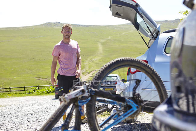 Ciclista con bota de bicicleta en coche mirando a la cámara sonriendo - foto de stock