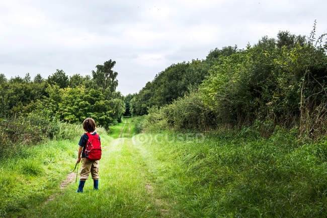 Visão traseira do menino com mochila na paisagem rural — Fotografia de Stock