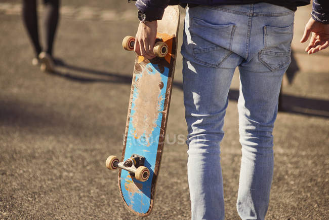 Молодой человек, гуляющий на открытом воздухе, со скейтбордом, вид сзади, низкая секция, Бристоль, Великобритания — стоковое фото