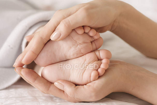 Mère tasses pieds bébé sur le lit — Photo de stock