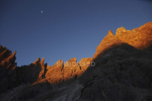Formations rocheuses couvertes de lumière du coucher du soleil avec lune dans le ciel — Photo de stock
