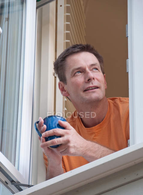 Mann mit Kaffee lehnt sich aus Fenster — Stockfoto