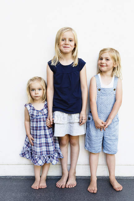 Retrato de tres hermanas jóvenes de pie frente a la pared blanca - foto de stock