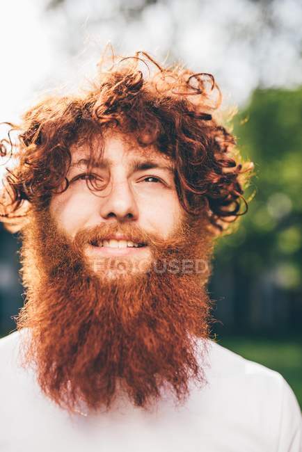 Portrait of young male hipster with curly red hair and beard  in park — Stock Photo