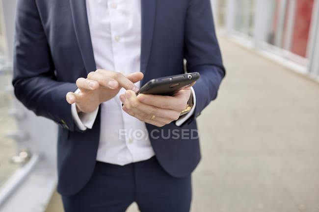 Mittelteil von Geschäftsmann auf Fußgängerbrücke SMS auf Smartphone, London, Großbritannien — Stockfoto