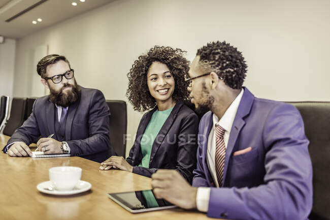Joven empresaria conversando en mesa de conferencias con hombres de negocios - foto de stock
