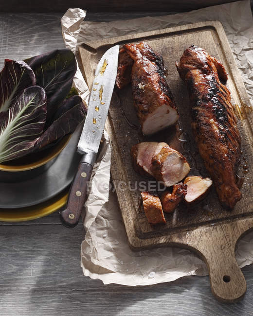 Lombo di maiale arrosto con coltello e foglie di radicchio in ciotola — Foto stock