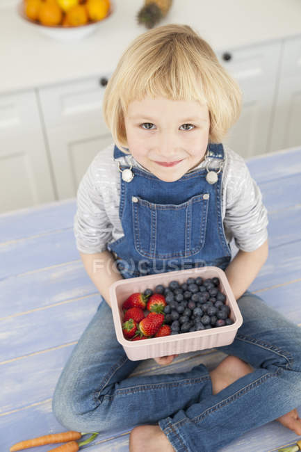 Portrait of cute girl holding punnet of blueberries and strawberries on kitchen counter — Stock Photo