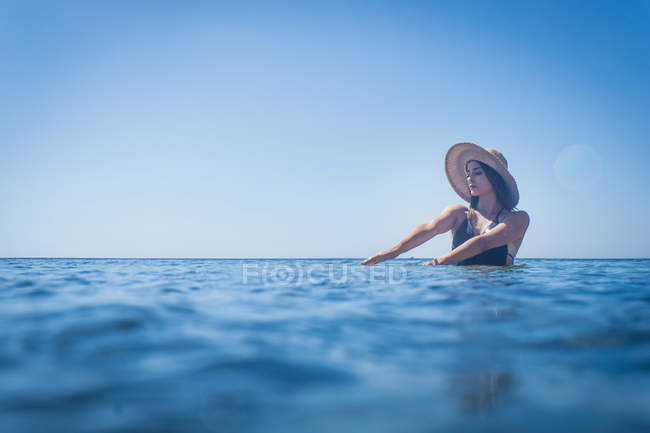 Jeune femme portant un chapeau de soleil pataugeant dans la mer bleu profond, Villasimius, Sardaigne, Italie — Photo de stock