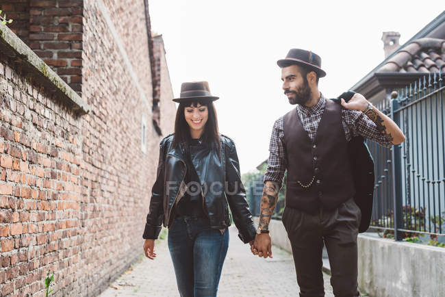 Jeune couple passant devant un mur de briques — Photo de stock