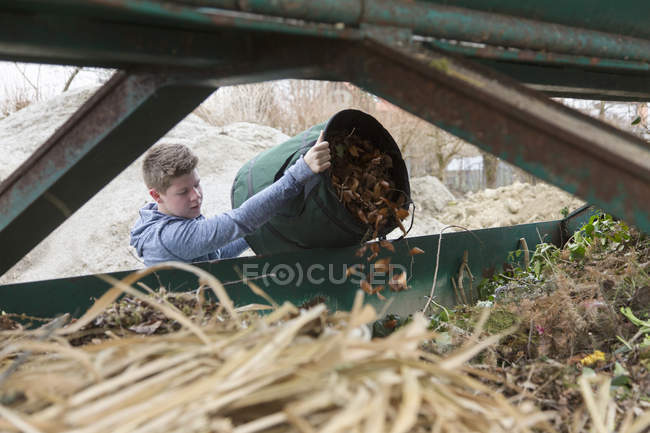 Мальчик-подросток выбрасывает садовые отходы в мусорное ведро — стоковое фото