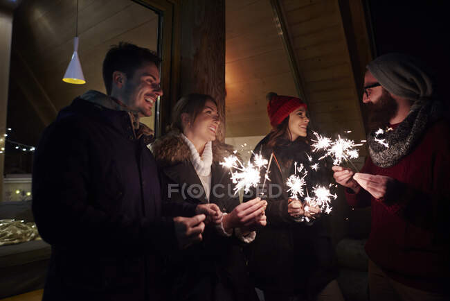 Friends playing with sparklers by chalet — Stock Photo