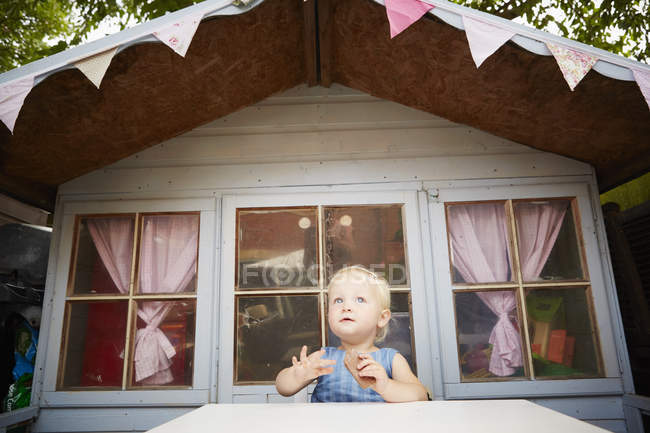 Menina sentada à mesa na frente da casa de brincar e olhando para longe — Fotografia de Stock