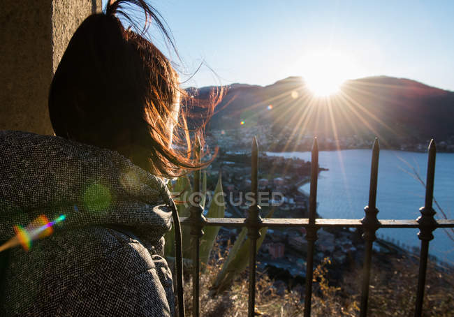 Vista elevada sobre el hombro de la mujer mirando hacia fuera sobre la costa al atardecer, Italia - foto de stock