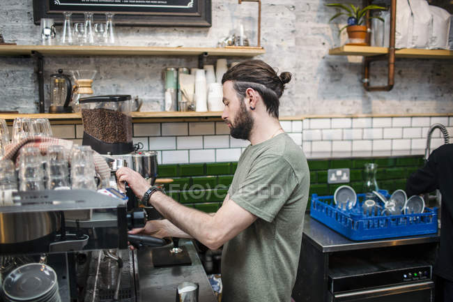 Joven barista masculino preparando café en la cocina cafetería - foto de stock