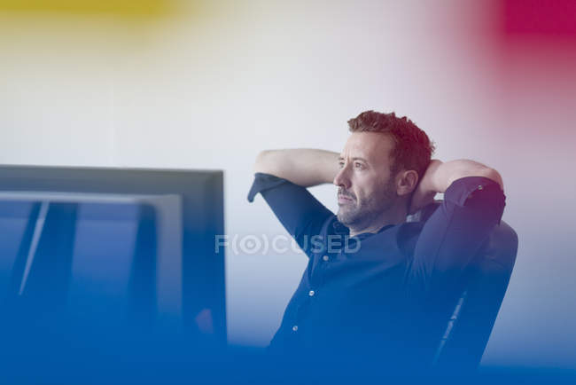 Handsome Caucasian businessman thinking with hands behind head and sitting in armchair in office — Stock Photo