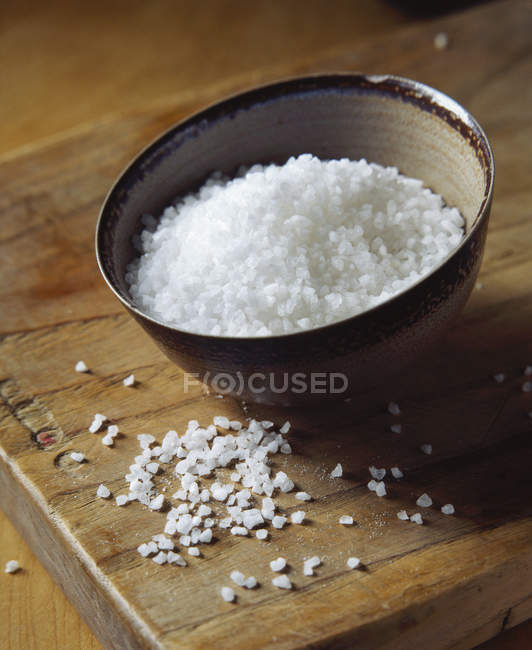 Натуральная морская соль в миске на деревянной доске — стоковое фото