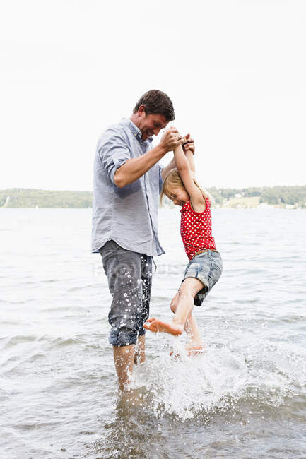 Hombre maduro levantando a su hija del lago Starnberg, Baviera, Alemania - foto de stock