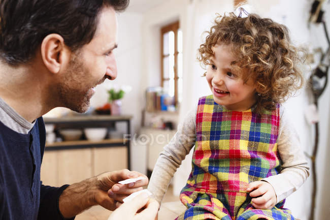 Зрілий чоловік показує дочку клейові штукатурки на кухні — стокове фото