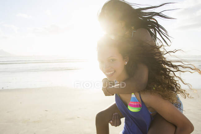 Retrato de jovem mulher piggybacking fêmea amigo na praia, Cidade Do Cabo, África do Sul — Fotografia de Stock