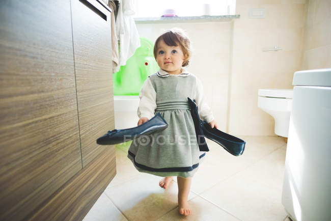 Female toddler carrying ladies shoes at home — Stock Photo