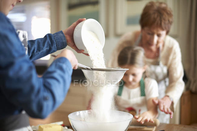 Senior woman and granddaughters sifting flour for cookies — Stock Photo