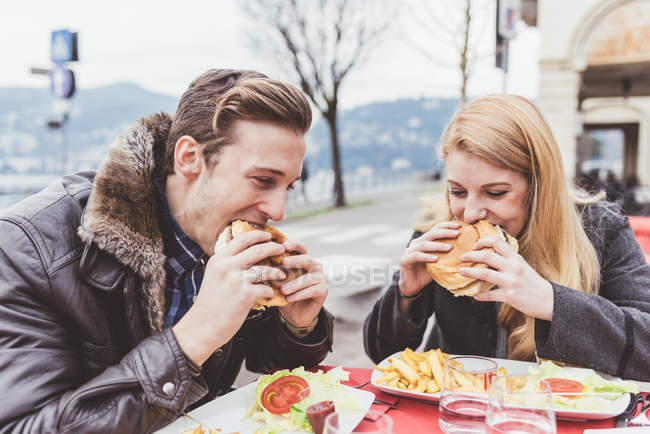 Young couple eating burgers at sidewalk cafe, Lake Como, Italy — Stock Photo