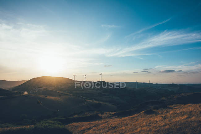 Puesta de sol sobre turbinas eólicas en el paisaje rodante - foto de stock
