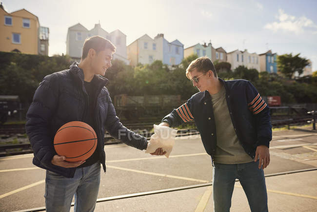 Jovem compartilhando saco de batatas fritas com amigo, jovem segurando basquete, Bristol, Reino Unido — Fotografia de Stock