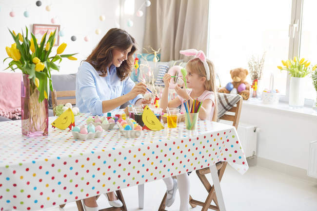 Menina e mãe pintando ovos de Páscoa à mesa — Fotografia de Stock