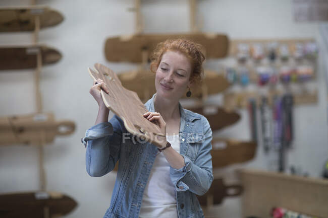 Mulher trabalhando na loja de skate, inspecionando tábua de madeira — Fotografia de Stock