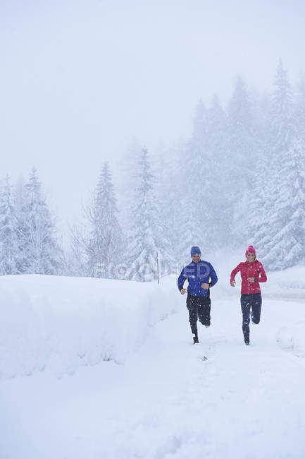 Happy sportive man and woman jogging in snow covered forest, Gstaad, Switzerland — Stock Photo