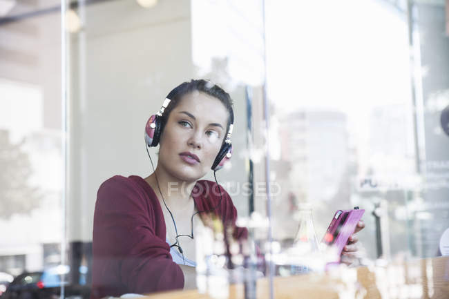 Jovem mulher sentada no café, usando fones de ouvido, segurando tablet digital — Fotografia de Stock