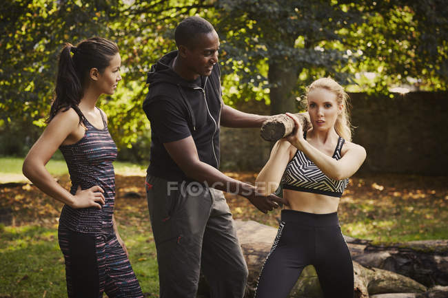 Two women with personal trainer explaining tree trunk shoulder lift in park — Stock Photo